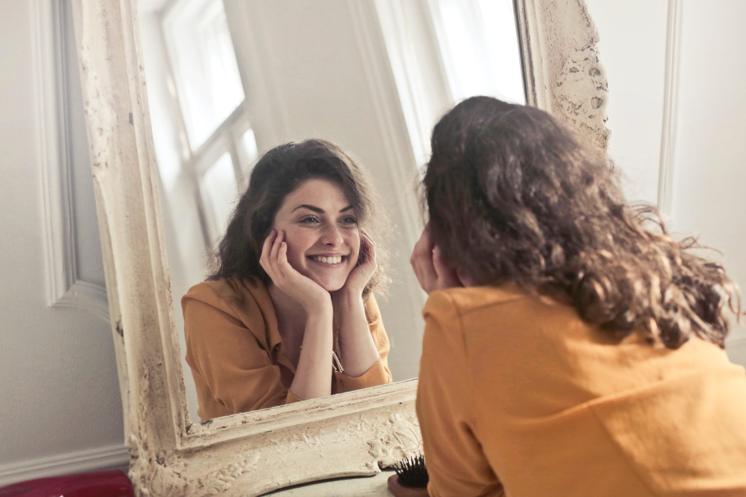 Woman smiling at her reflection - For many, falling off the wagon on a resolution can lead to self-doubt - this is why this is the perfect time to talk about building your self-worth!