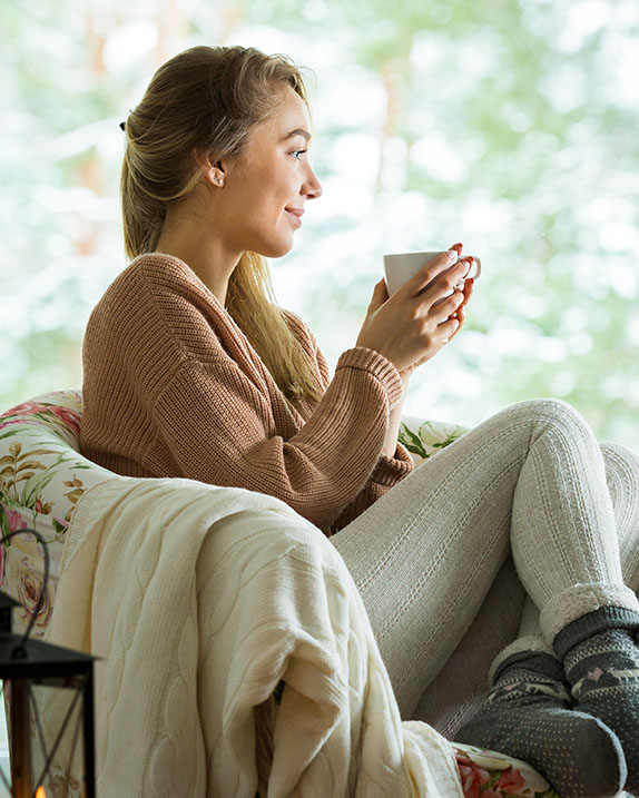 Young woman sitting home in a chair by the window with cup of ho Anxiety Treatment has helped this woman to be able to sit and enjoy her morning coffee